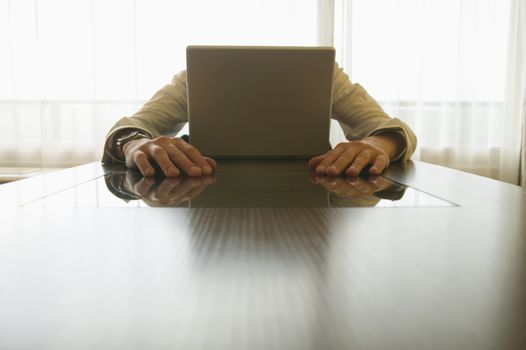 Caucasian businessman hiding behind laptop themes of frustration despair unrecognisable