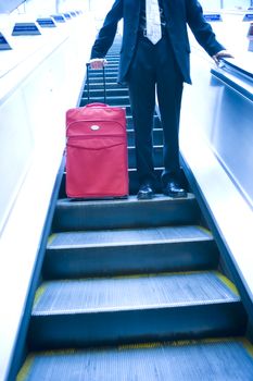 Businessman with suit case travelling down an escalator themes of departure travel deadlines arrival