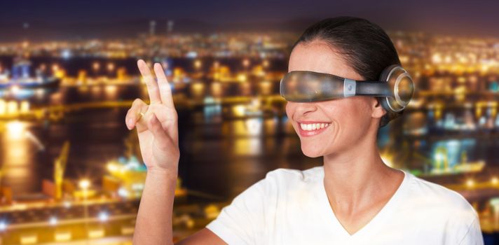 Smiling woman gesturing while using virtual video glasses against illuminated harbor against cityscape