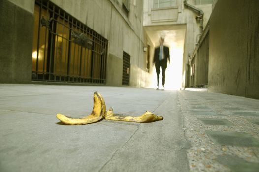 Low angle view of a businessman walking towards a banana skin themes of careless danger risk