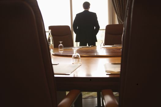 Businessman looking out of a
Boardroom window with his hands in 
his pockets themes of despair solitude contemplation