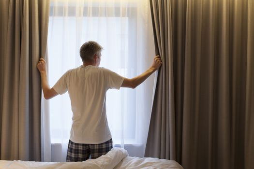 Businessman opening curtains in hotel room