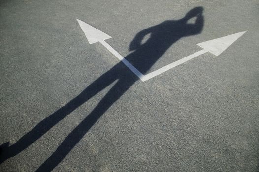 A businessman standing over a pair of road arrows while scratching his head themes of confusion direction decision