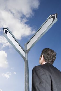 Caucasian businessman standing in front of a blank road sign themes of direction choice future