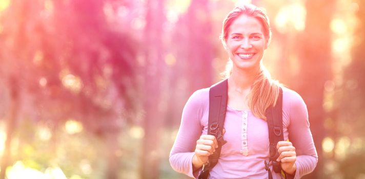 Portrait of smiling woman standing in forest carrying backpack