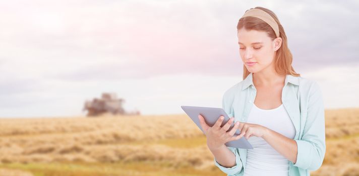 Pretty hipster using tablet  against harvester working on farm