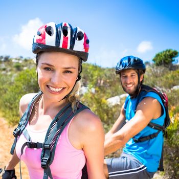 Fit couple cycling up mountain trail smiling on a sunny day