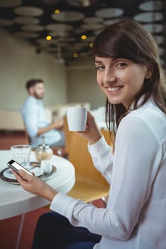 Portrait of executive using mobile phone while having coffee in cafÃ©