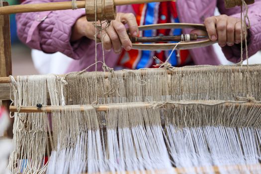 Grandmother works behind an old spinning machine.Spice on an old spinning wheel. Ancient fabrication. Woman weaver