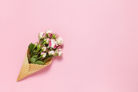 Small roses in waffle cone on pink background, copy space. Minimal style flat lay. For greeting card, invitation. March 8, February 14, birthday, Valentine's, Mother's, Women's day concept. Top view.