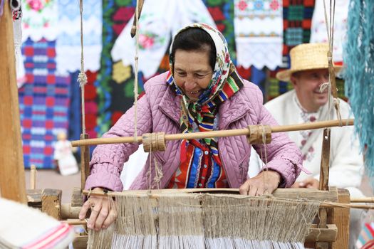 Grandmother works behind an old spinning machine.Spice on an old spinning wheel. Ancient fabrication. Woman weaver