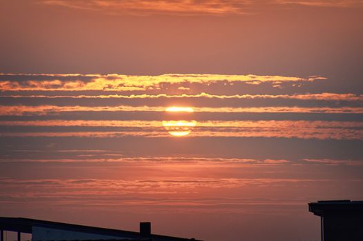 Red sunset over rooftop silhouettes in the late evening with clouds covering the sun