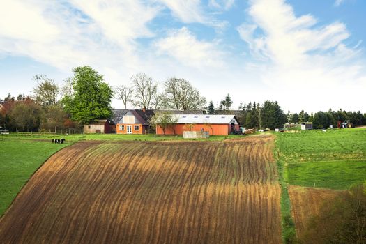 Farm on the top of a hill with cultivated fields under a blue sky