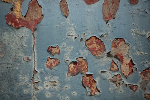 Weathered blue wall with pealing paint on a rusty surface in red color