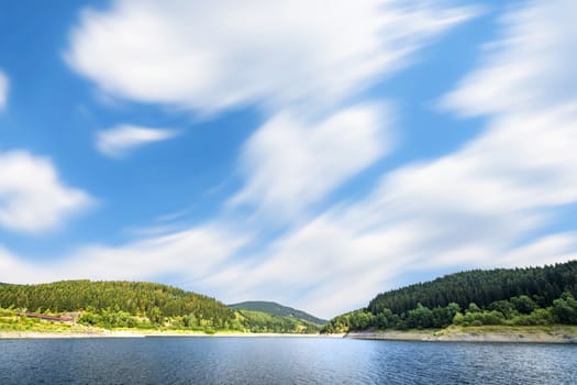 Large lake under a blue sky in the wind with forest on the shore in the summer