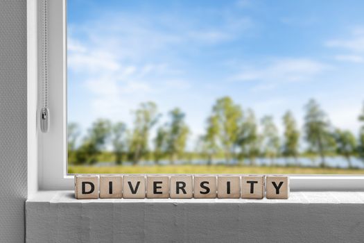 Diversity word in a window sill with a garden in the spring with green trees under a blue sky