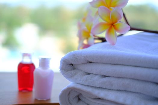 Close up of Stack of towels with fresh Plumeria flowers decor and little bottles of shampoo and hair conditioner. Wellness concept. 