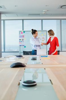 Smiling business colleagues shaking hands in conference room in office