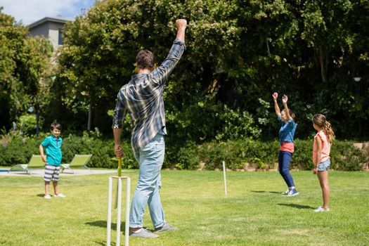 Family playing cricket in park on a sunny day