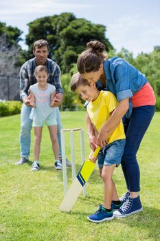 Family playing cricket in park on a sunny day