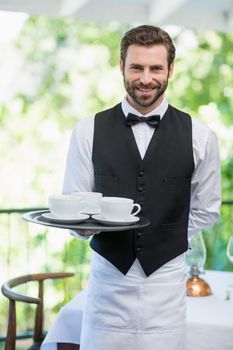 Portrait of male waiter holding tray with coffee cups in restaurant