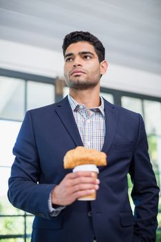 Businessman holding disposable coffee cup and croissant in a restaurant