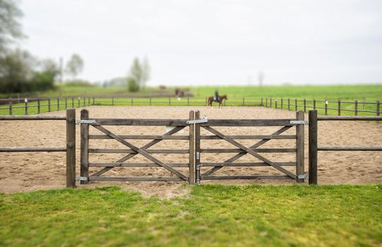 Wooden gate to an equine training course in a misty weather with green grass around the track