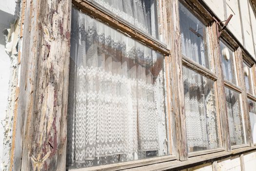 Old wooden windows on a row with white vintage curtains in a village