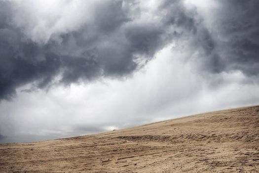 Sandstorm in a dry desert under a cloudy sky with dark clouds