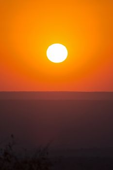 Large red sunset over silhouettes of hills in a canyon in the late summer