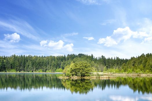 Colorful lake scenery with reflections of trees in the water and with a small island in the middle