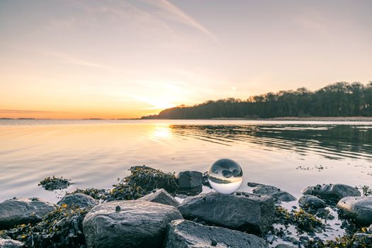 Glass orb on o rock by the lake in a beautiful sunrise an early morning