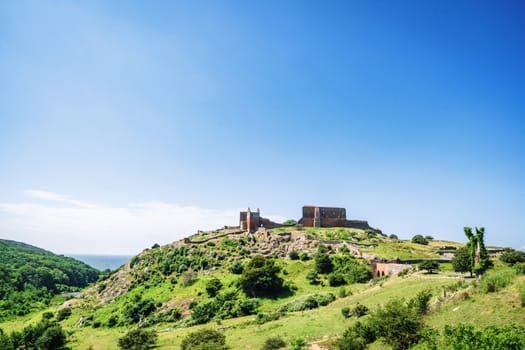 Ruin of a castle on the top af o green hill in the summer under a blue sky