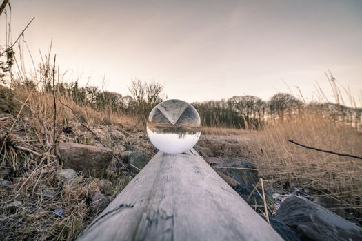 Crystal ball in balance on a wooden log in the nature by a lake