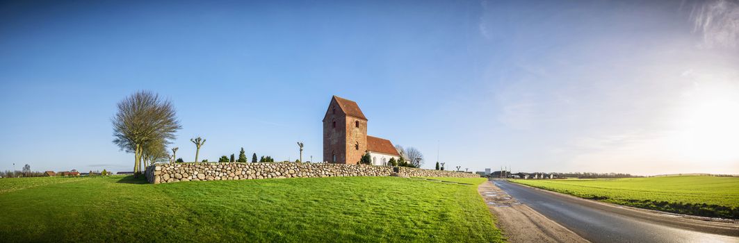 Panorama landscape with a church in rural surroundings under a blue sky in Scandinavia