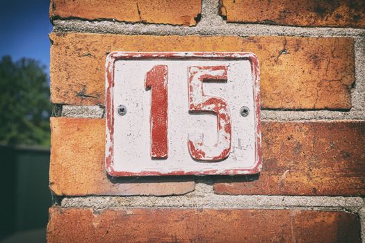 Street number 15 on a sign with pealing paint on a brick house in a street