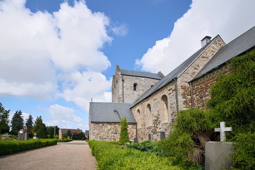 Tombstone with a cross in front of a church under a blue sky in the daytime