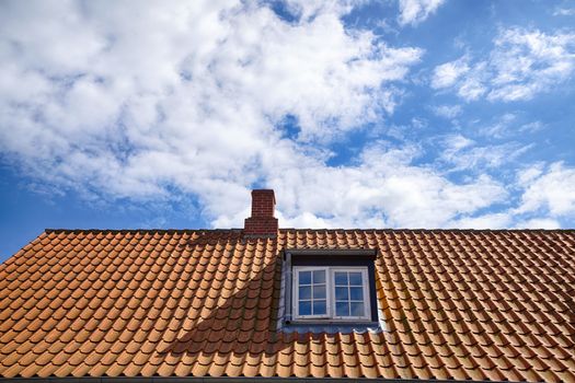 Tiled red roof with a rooftop window and a small chimney under a blue sky in the summer
