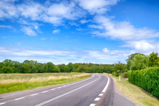 Curvy road under a blue sky in the summer with fields and trees by the roadside
