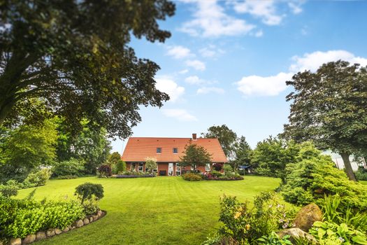 Red brick house in a beautiful garden in the summer with a green lawn under a blue sky