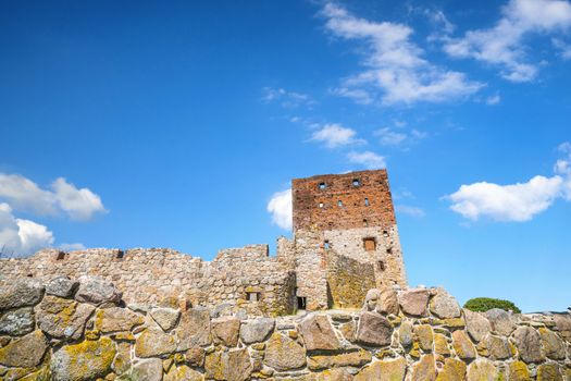 Castle ruin rising up behind an old brick wall in the summer under a blue sky