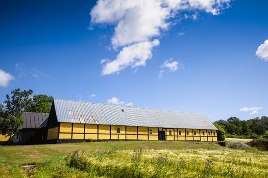 Yellow barn on a green meadow in the summertime under a blue sky