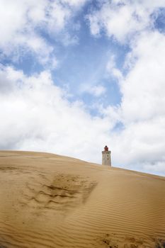 Lighthouse rising up behind a sand dune under a blue heaven with fluffy white clouds