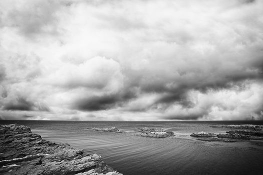 Cliffs by the shore of the sea with dramatic dark clouds coming in monochrome tone