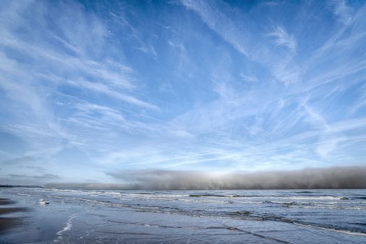 Dark clouds coming in over the sea under a blue sky with waves on the beach