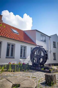 Water mill with flowers on a terrace in a backyard with white buildings