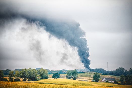 Black smoke from a fire in a rural countryside landscape with fields and trees