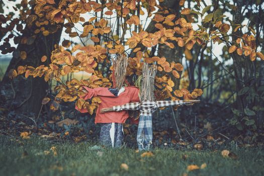 Scarecrows in a garden in the fall with autumn leaves hanging above