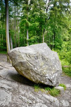 Large rock in a green forest in the summer with solid ground under the large stone