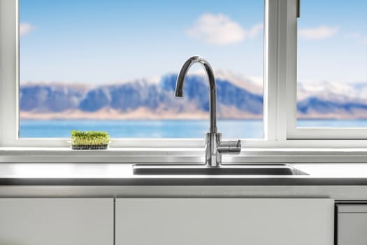 Kitchen sink by a window with a view over the sea and mountains with green cress growing